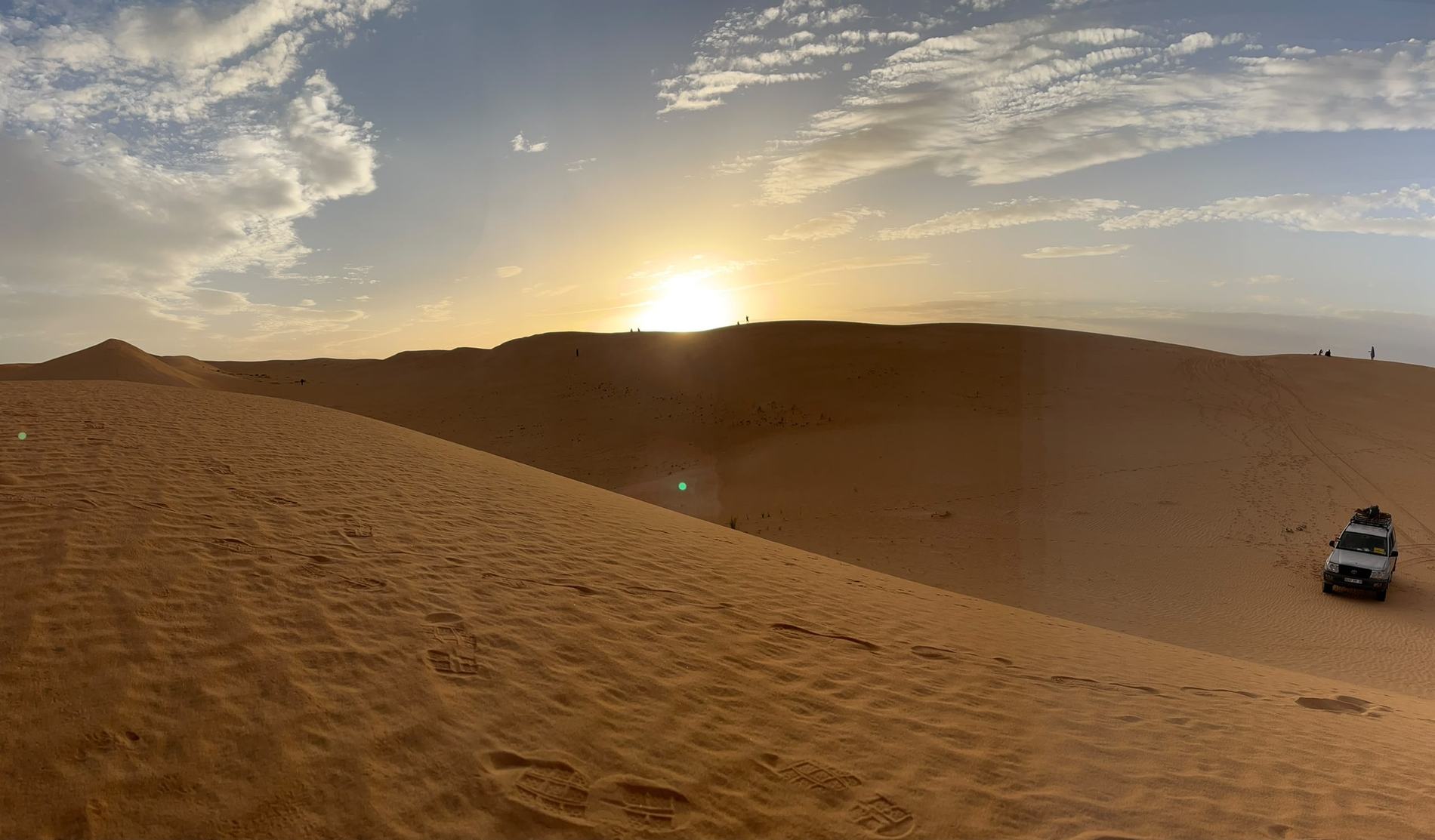 Amanecer sobre las dunas del Sáhara, con un todoterreno en la ladera