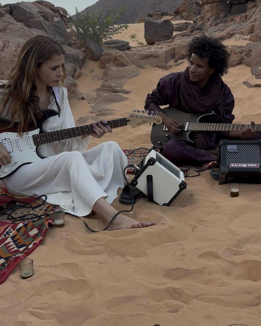 Mar Sánchez y Khily Ag Osman tocando guitarras eléctricas en la arena, entre las rocas del Sáhara