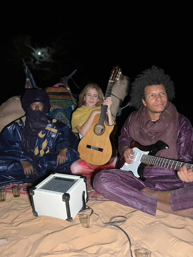Mar Sánchez con guitarra española junto a Khily Ag Osman y otro músico, de noche en el desierto bajo la luna